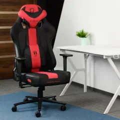 Czarno-czerwone krzesło gamingowe Diablo Chairs Player na tle białego biurka i drzwi.