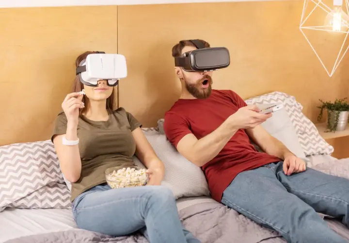 Para ogląda filmy VR na kanapie, trzymając popcorn i pilota.