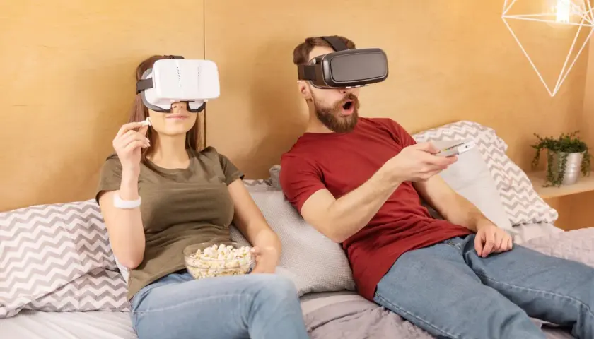 Para ogląda filmy VR na kanapie, trzymając popcorn i pilota.