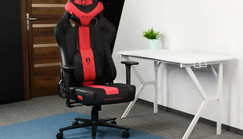 Czarno-czerwone krzesło gamingowe Diablo Chairs Player na tle białego biurka i drzwi.